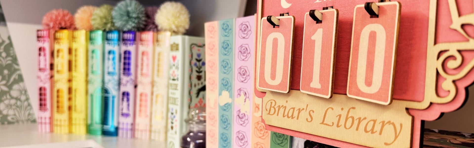 Reading nook ideas with pastel special edition books, pom-pom bookmarks, and a pink wooden “Briar’s Library” shelf sign in a cozy bookish corner.