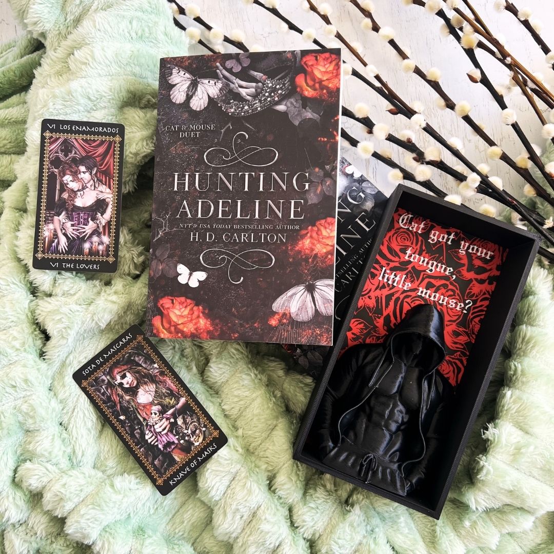 Hunting Adeline by H.D. Carlton book flat lay with tarot cards, pussy willow branches and a black Zade Meadows “Cat got your tongue, little mouse?” display box.